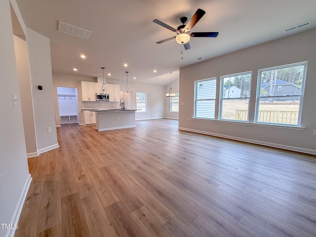 unfurnished living room with sink, ceiling fan with notable chandelier, and light hardwood / wood-style flooring