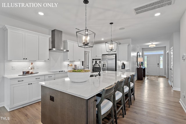 kitchen featuring white cabinetry, hanging light fixtures, a kitchen island with sink, stainless steel refrigerator with ice dispenser, and wall chimney exhaust hood