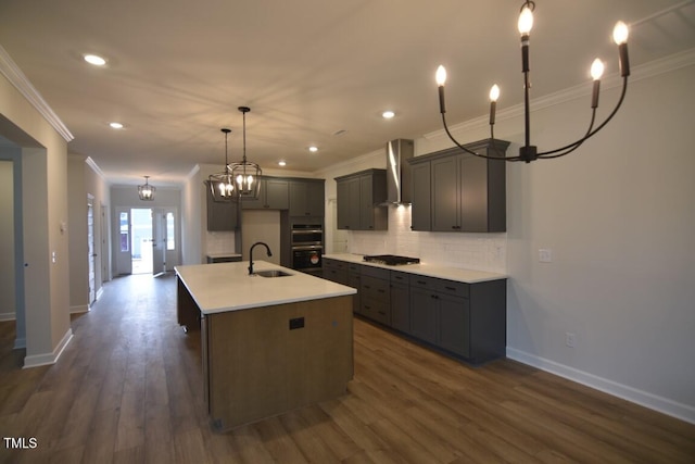 kitchen featuring gas stovetop, tasteful backsplash, a kitchen island with sink, wall chimney range hood, and sink