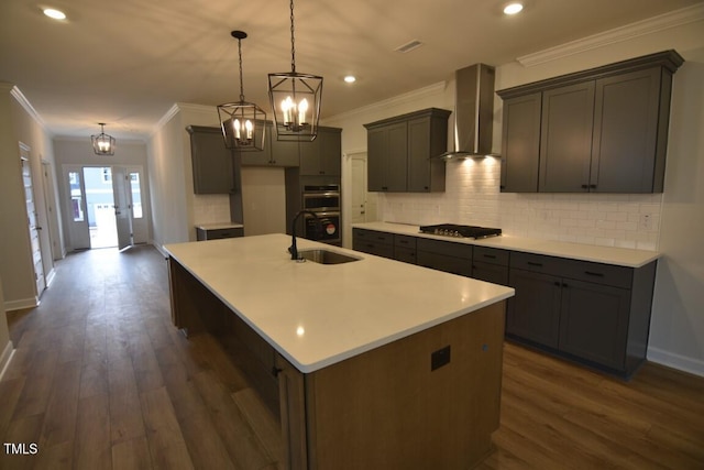 kitchen featuring pendant lighting, sink, wall chimney range hood, and a center island with sink