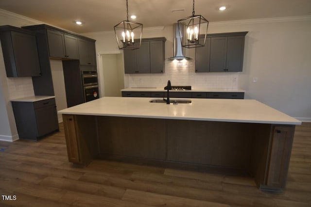 kitchen featuring dark hardwood / wood-style floors, hanging light fixtures, sink, an island with sink, and wall chimney exhaust hood