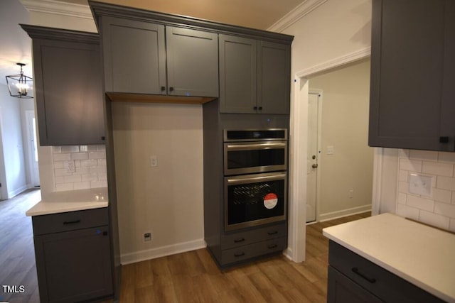 kitchen featuring decorative backsplash, light wood-type flooring, an inviting chandelier, ornamental molding, and double oven