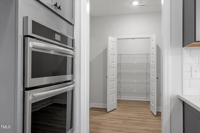 kitchen with backsplash, stainless steel double oven, light hardwood / wood-style floors, and gray cabinetry