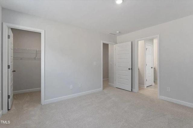 unfurnished bedroom featuring a spacious closet, light colored carpet, and a closet