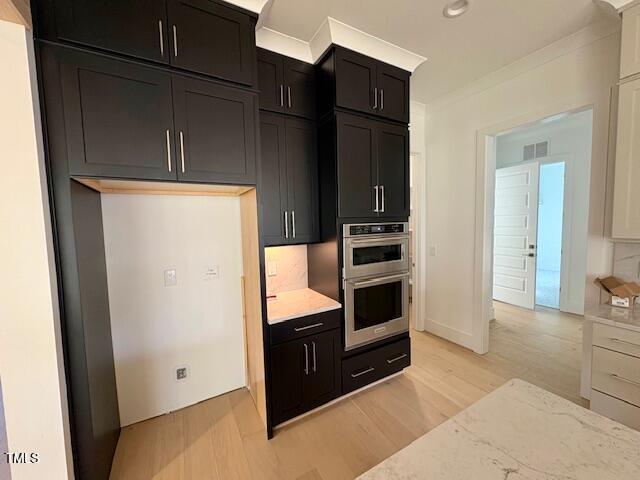 kitchen featuring crown molding, stainless steel double oven, light stone countertops, light hardwood / wood-style floors, and decorative backsplash