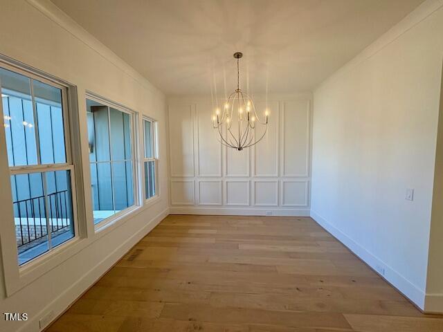 unfurnished dining area with ornamental molding, light hardwood / wood-style flooring, and a notable chandelier