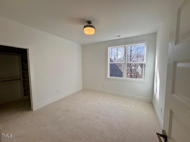 unfurnished bedroom featuring a spacious closet, light carpet, and a closet