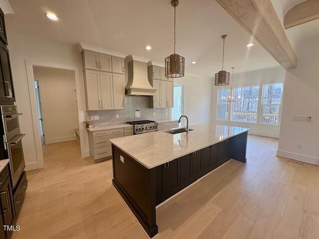 kitchen with pendant lighting, an island with sink, sink, stainless steel appliances, and custom range hood