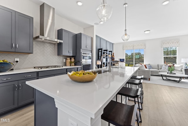 kitchen featuring gray cabinets, an island with sink, sink, and wall chimney range hood