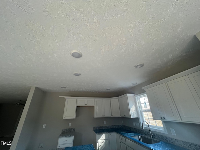 kitchen with sink, white cabinets, and a textured ceiling