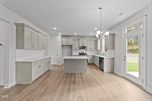 kitchen with gray cabinetry, appliances with stainless steel finishes, light hardwood / wood-style floors, and a center island