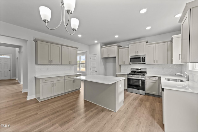 kitchen with stainless steel appliances, decorative light fixtures, gray cabinetry, and light hardwood / wood-style flooring