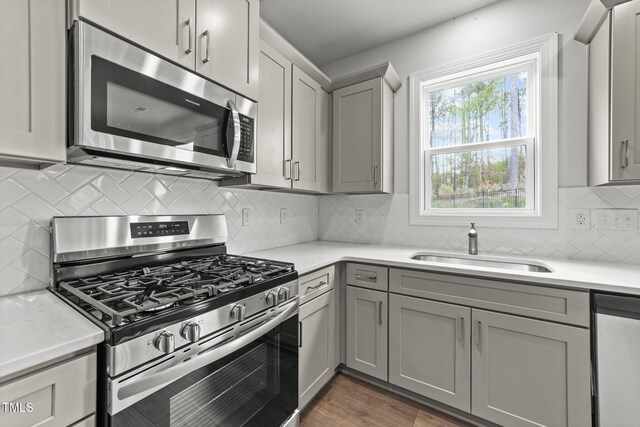 kitchen featuring stainless steel appliances, sink, dark hardwood / wood-style flooring, gray cabinetry, and decorative backsplash