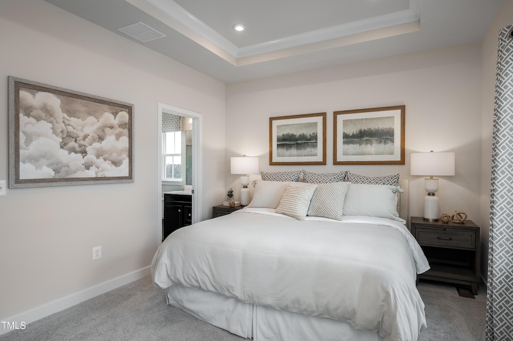 bedroom with light carpet, a tray ceiling, ornamental molding, and ensuite bathroom