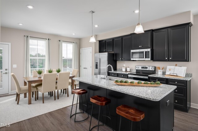 kitchen featuring dark hardwood / wood-style floors, pendant lighting, an island with sink, a kitchen bar, and stainless steel appliances