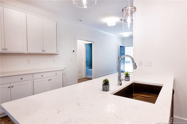 kitchen with hanging light fixtures, white cabinetry, light stone countertops, and sink