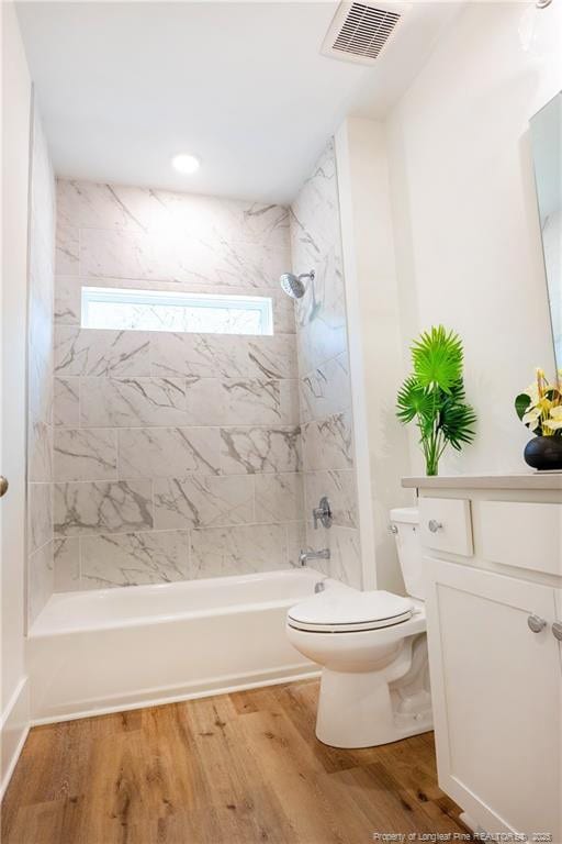 full bathroom with tiled shower / bath combo, vanity, hardwood / wood-style floors, and toilet