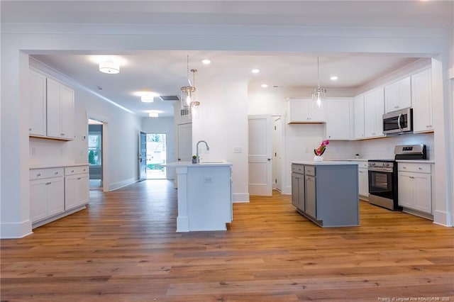 kitchen with white cabinetry, appliances with stainless steel finishes, hanging light fixtures, and a center island with sink