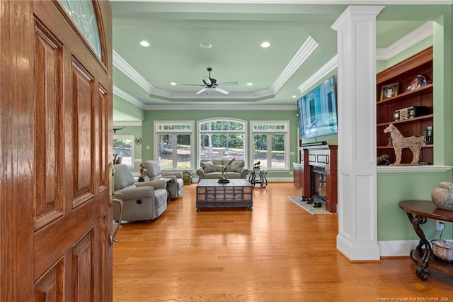 living room with a fireplace with flush hearth, light wood-style flooring, a tray ceiling, decorative columns, and ceiling fan