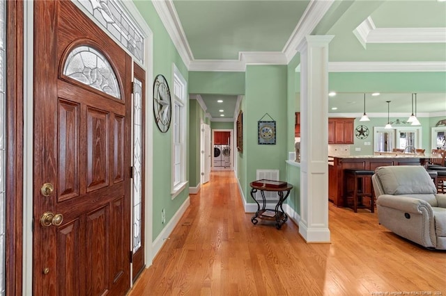 foyer entrance with light wood-style flooring, crown molding, and decorative columns
