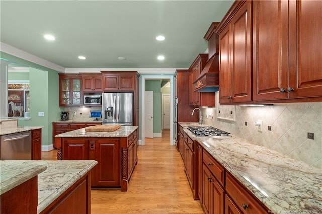kitchen with light wood finished floors, crown molding, light stone countertops, appliances with stainless steel finishes, and custom exhaust hood