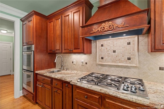 kitchen featuring light stone countertops, premium range hood, stainless steel appliances, a sink, and crown molding
