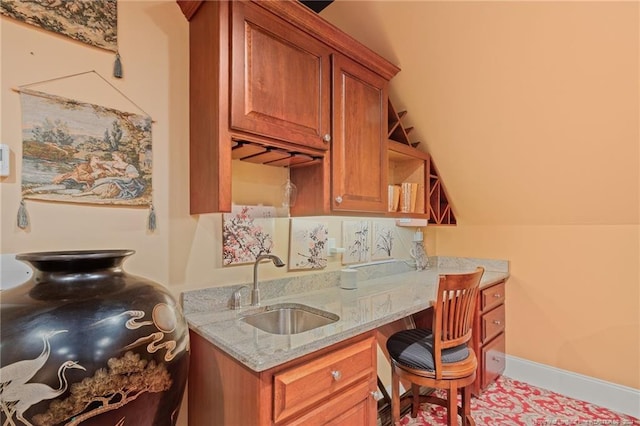 kitchen featuring light stone counters, brown cabinets, open shelves, and a sink