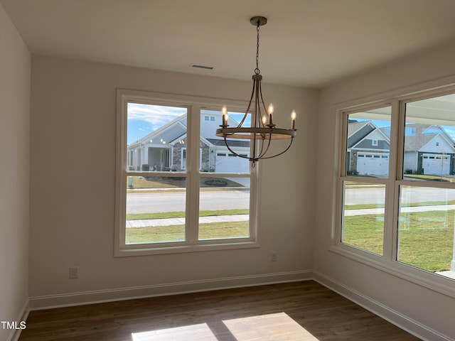 unfurnished dining area with dark hardwood / wood-style flooring, an inviting chandelier, and a healthy amount of sunlight