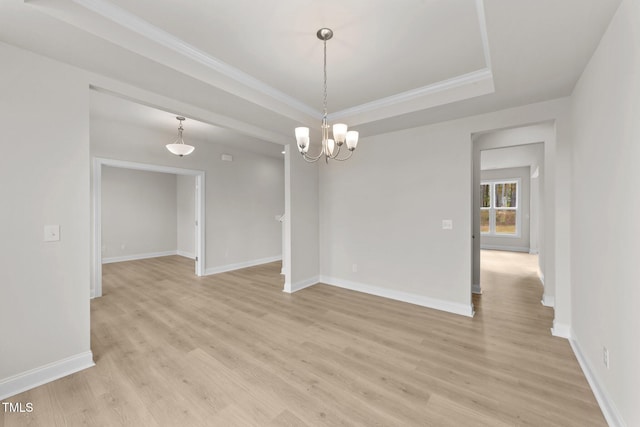 empty room featuring light wood-type flooring, a chandelier, ornamental molding, and a raised ceiling