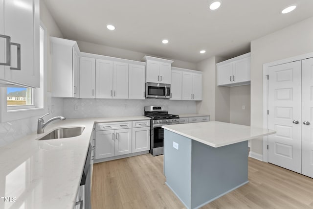 kitchen featuring light hardwood / wood-style floors, white cabinetry, sink, appliances with stainless steel finishes, and a center island