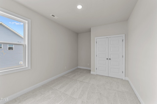 unfurnished bedroom with light colored carpet and a closet