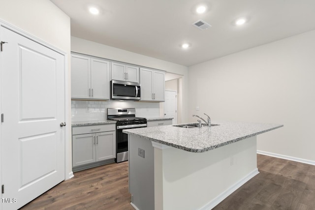 kitchen with sink, gray cabinets, appliances with stainless steel finishes, light stone countertops, and an island with sink