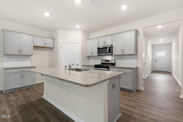 kitchen with sink, gray cabinets, a kitchen island with sink, stainless steel appliances, and dark hardwood / wood-style floors