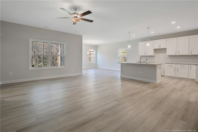 unfurnished living room featuring ceiling fan with notable chandelier, light wood finished floors, recessed lighting, and baseboards