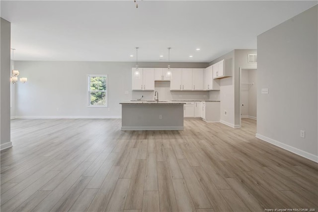 kitchen with light wood-style floors, white cabinetry, pendant lighting, and a sink