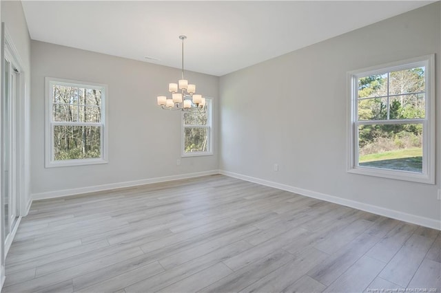 empty room featuring baseboards, a notable chandelier, and light wood finished floors