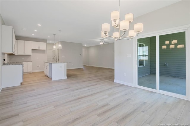 kitchen featuring light wood finished floors, hanging light fixtures, open floor plan, a kitchen island with sink, and white cabinets