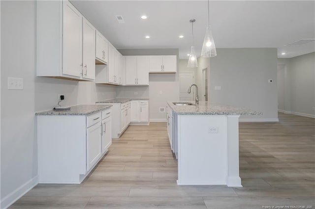 kitchen with an island with sink, white cabinetry, a sink, and decorative light fixtures