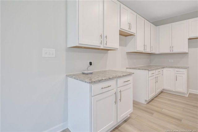 kitchen featuring light stone countertops, light wood-style floors, baseboards, and white cabinetry