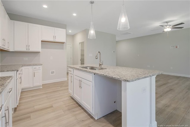 kitchen featuring white cabinets, a sink, hanging light fixtures, and a center island with sink