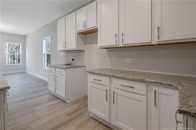 kitchen with light wood-type flooring, baseboards, white cabinetry, and light stone counters