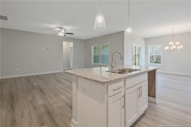 kitchen with open floor plan, a kitchen island with sink, a sink, and white cabinets