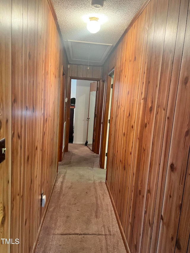 hall featuring light carpet, a textured ceiling, and wooden walls