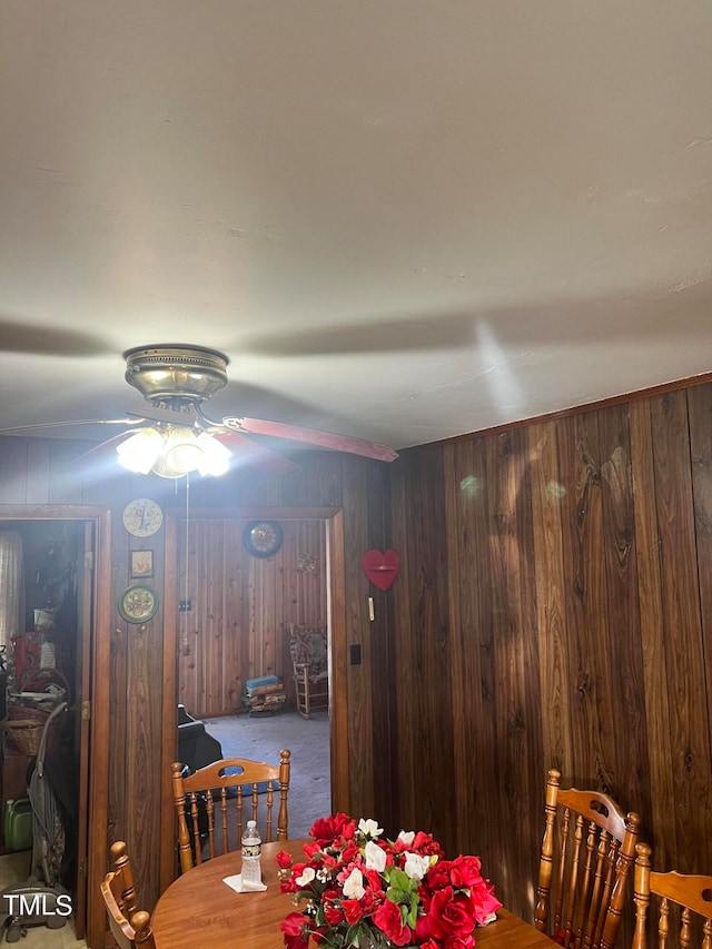 carpeted dining room featuring wood walls and ceiling fan