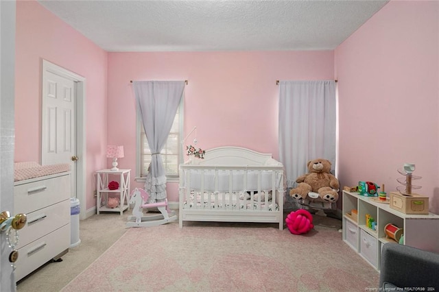 bedroom featuring light carpet, a nursery area, and a textured ceiling