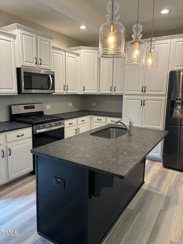 kitchen with light wood-type flooring, appliances with stainless steel finishes, white cabinetry, sink, and an island with sink