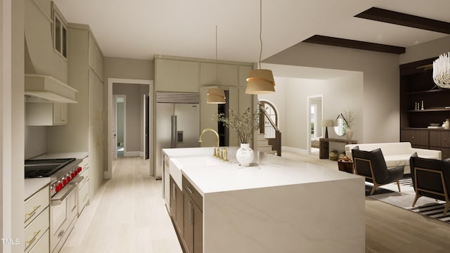 kitchen with light wood-style floors, built in refrigerator, stainless steel gas cooktop, a kitchen island with sink, and a sink