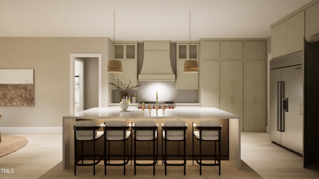 kitchen featuring light wood-style flooring, a kitchen island with sink, premium range hood, a breakfast bar area, and stainless steel built in fridge