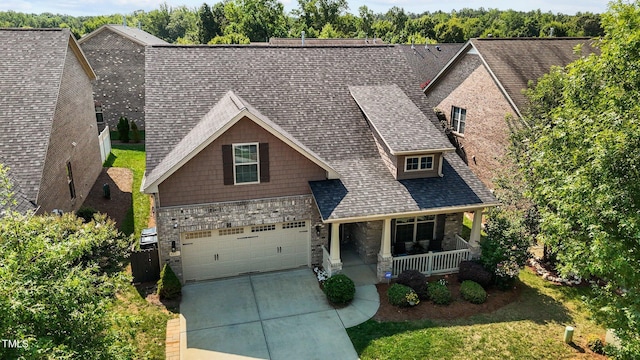 craftsman-style home with driveway, stone siding, covered porch, and roof with shingles
