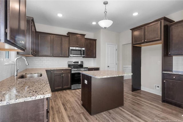 kitchen with sink, hardwood / wood-style flooring, appliances with stainless steel finishes, decorative light fixtures, and a kitchen island